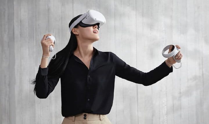 A person wearing and using an Oculus Quest 2 VR headset in front of a gray background.